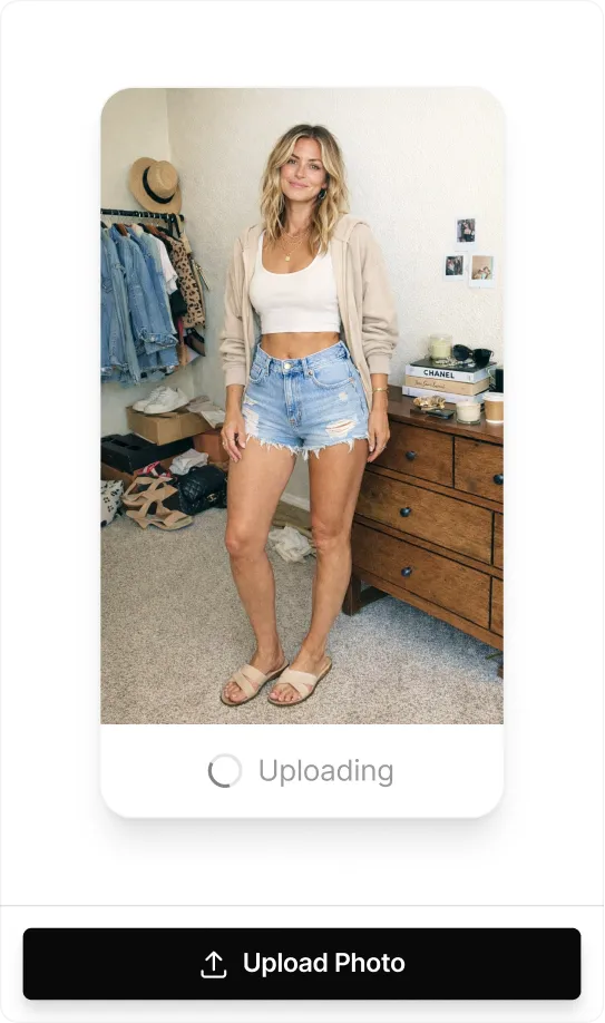 Woman smiling in a beige hoodie, white crop top, denim shorts, and beige sandals.